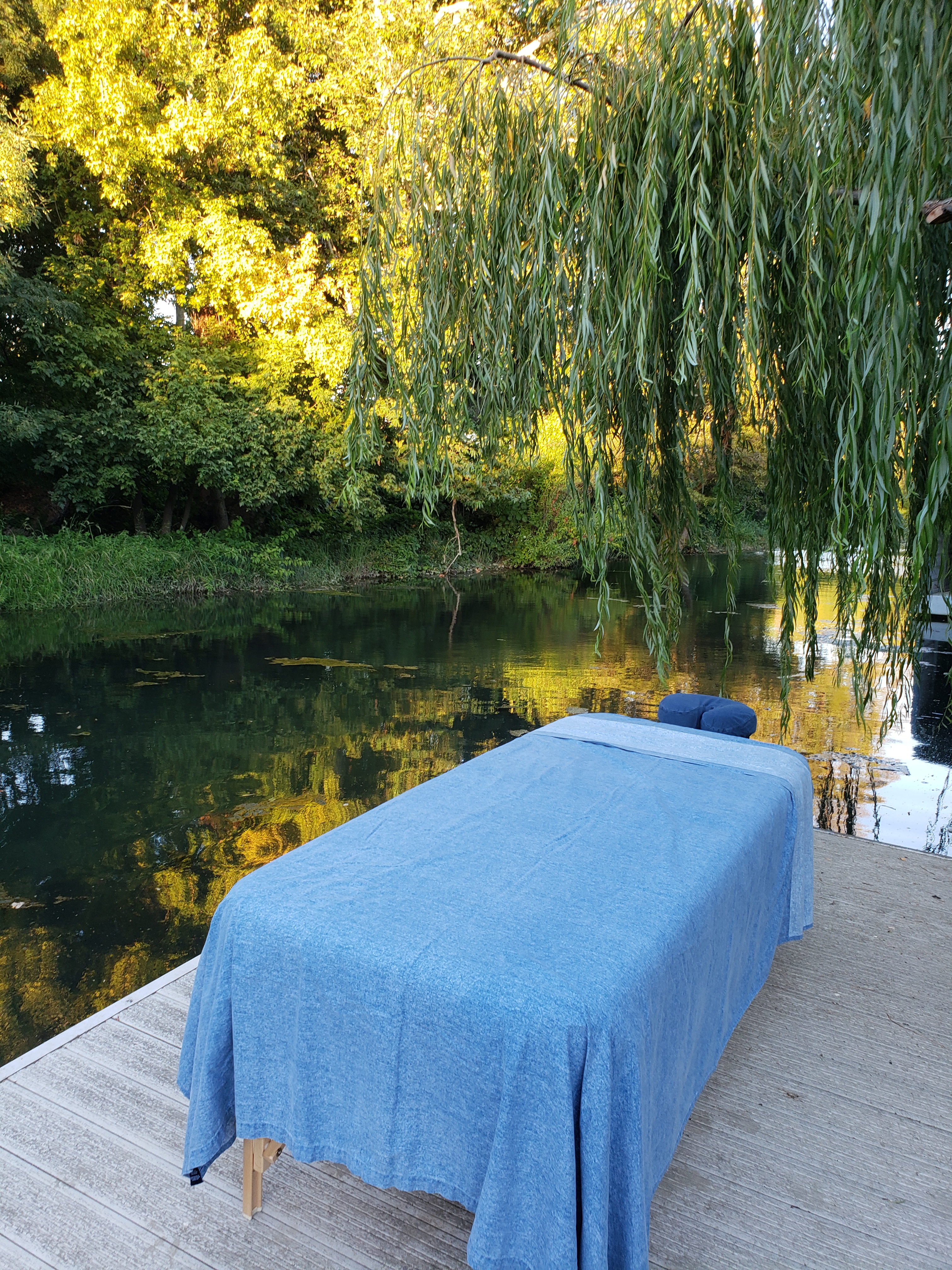 Massage table set up on a dock in the Delta near Isleton, CA. Water is calm and massage table is under a willow tree.